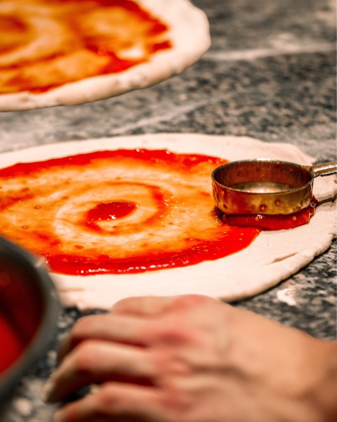 Sauce tomate étalée à la louche sur une pâte à pizza dans la cuisine de la Trattoria Bella