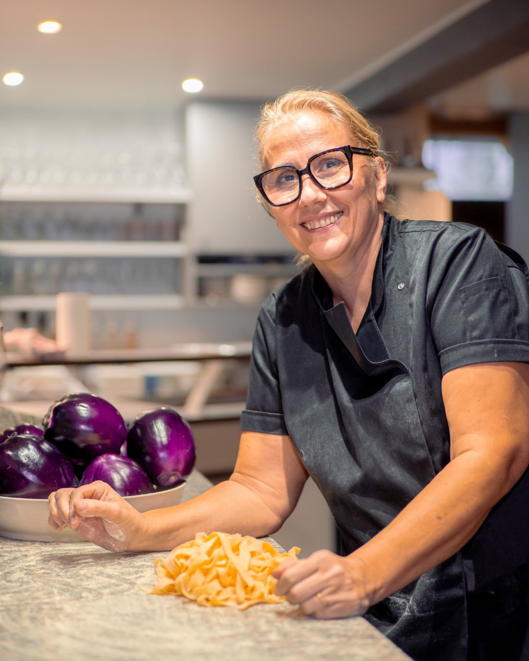 Rose en cuisine à la Trattoria Bella, devant des pâtes fraîches et des aubergines